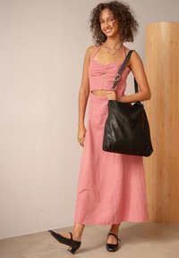 Rosa linne maxiklänning med figursydd kropp, knapppdetaljer och skuren midja. Svart läderaxelväska och svarta låga klackskor.