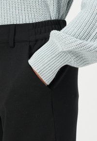 Lichtblauwe gebreide trui met geribde manchetten, gecombineerd met zwarte broeken met een elastische tailleband en zijzakken.