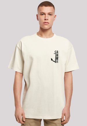 Cream-colored cotton t-shirt with a relaxed fit, short sleeves, and a graphic print featuring text and an anchor on the left side.