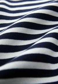 Gros plan d'un tissu côtelé à rayures horizontales bleu marine et blanc avec texture et plis visibles.