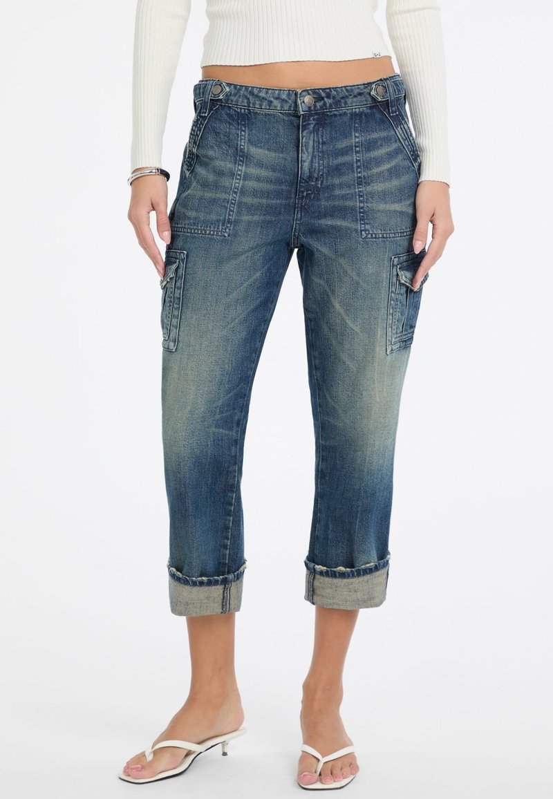 Blaue Denim-Cargohosen mit umgeschlagenen Säumen, Fronttaschen und seitlichen aufgesetzten Taschen. Der Stoff zeigt eine ausgewaschene Optik und eine strukturierte Oberfläche.