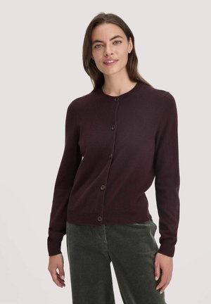 Bordeauxfarbener Strickcardigan mit rundem Ausschnitt, langen Ärmeln und frontalen Knöpfen. Weicher Stoff und gerippter Saum. Trägt man über grünen Cordhosen.
