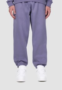 Purple sweatpants made of soft fabric, featuring elastic cuffs and a relaxed fit. Paired with white sneakers.