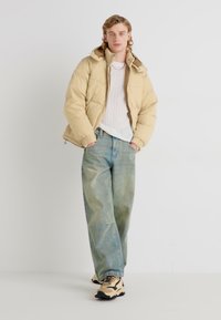 Beige puffer jacket with a high collar, layered over a white knitted sweater, paired with light-wash loose jeans and black-accented sneakers.