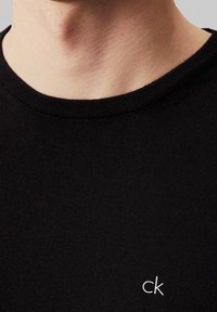 Zwart katoenen T-shirt met een ronde hals en korte mouwen, voorzien van een klein wit "ck"-logo op de borst. Soepele textuur.