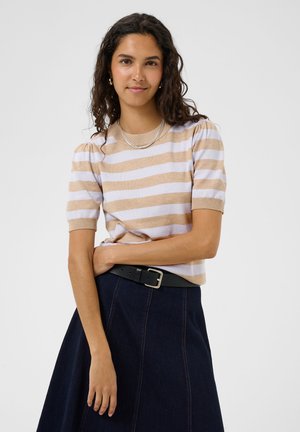 Ung kvinde med krøllet hår iført en beige og hvid stribet kortærmet sweater, mørkt denimskørt, sort bælte og sølvhalskæder.