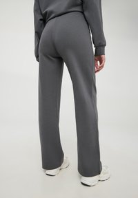 Szare, wysokie spodnie dresowe o luźnym kroju, z gładką fakturą i prostym wzorem. Noszone z białymi butami sportowymi.