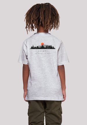 Child with dreadlocks wearing a gray t-shirt with a back print of a mountain skyline and an orange sun above the word "ESCAPE."