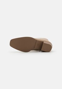 Beige potītes zābaki ar teksturētu brūnu gumijas zoli. Rūpīgi noformēta apaļa purngala forma un minimālas šuvju detaļas. Gluda sintētiskā virsma.