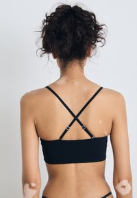 Soutien-gorge de sport noir au design ajusté, doté de bretelles croisées et réglables, avec une texture lisse. Le dos est uni avec un minimum de détails.