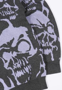 Ciemnoszary dzianinowy materiał z dużymi, jasnopurpurowymi wzorami czaszek oraz prążkowanymi mankietami na rękawach.