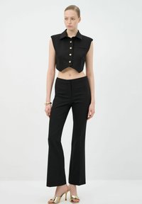 Black cropped sleeveless shirt with gold buttons, paired with tailored black flared pants. Model wearing metallic gold heeled sandals.