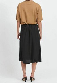 T-shirt marron surdimensionné associé à une jupe midi noire. La jupe possède une taille élastique et une texture douce et fluide. Des talons noirs complètent l'ensemble.