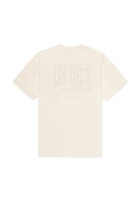 Μπεζ βαμβακερό μπλουζάκι με κοντά μανίκια. Στην πλάτη υπάρχει ένα ξεθωριασμένο γραφικό κείμενο με τη φράση "LES DEUX GOODS."