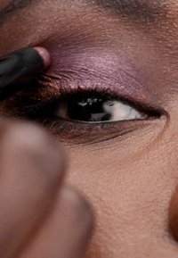 Applicazione del trucco per gli occhi con un riflesso viola profondo sulla palpebra, accentuato da una matita eyeliner nera, con attenzione all'area degli occhi.
