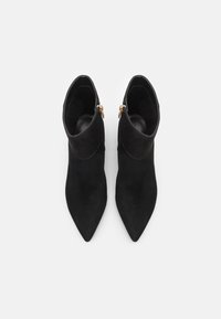 Stivali ankle in suede nero con punta a punta e design con risvolto. Gli accessori in metallo dorato alle cerniere aggiungono dettagli alla silhouette elegante.