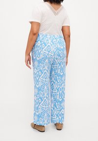 Modré a bílé vzorované kalhoty s širokým střihem, elastickým pasem a hladkým povrchem, spojené s jednoduchým bílým tričkem s krátkým rukávem.