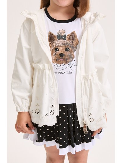 Παιδί που φοράει λευκό μπουφάν με κεντήματα, λευκό πουκάμισο με πρόσωπο σκύλου από παγιέτες και μαύρη φούστα με πουά.