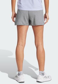 Pantalones cortos deportivos grises con un patrón texturizado, que presentan un ajuste relajado y un dobladillo que cae a mitad del muslo, combinados con zapatillas deportivas blancas.
