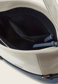 Borsa a mano in pelle con texture crema e un interno in tessuto scuro. Presenta una tasca con zip e un accento in pelle blu. Visibile il dettaglio delle cuciture.