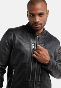 Veste en cuir noir avec un motif crocodile texturé, fermeture éclair frontale et accents en métal argenté. Col côtelé et design ajusté.