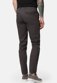 Ciemnoszare bawełniane spodnie o dopasowanym kroju, z tylnymi kieszeniami zapinanymi na guziki oraz delikatną fakturą. Noszone z szarymi trampkami.