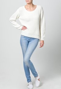 White knitted sweater with a wide neckline, paired with light blue skinny jeans and white sneakers. The sweater features ribbed texture.