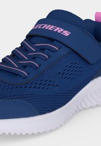 Chaussure de sport bleue avec des accents roses, tige en mesh, lacets élastiques, bride Velcro avec le logo Skechers et semelle blanche texturée.