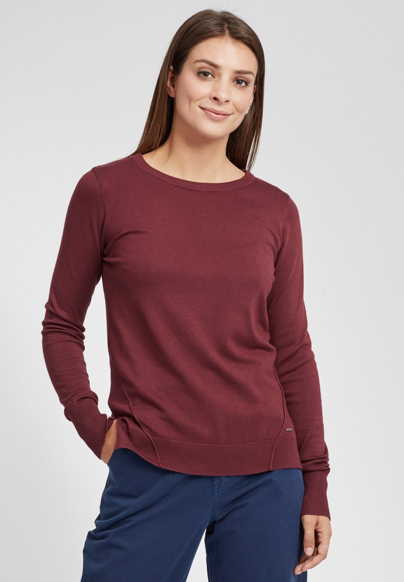 Maglione a maniche lunghe bordeaux con scollo rotondo, polsini e orlo a coste. Presenta spacchi laterali e un piccolo logo accanto all'orlo.