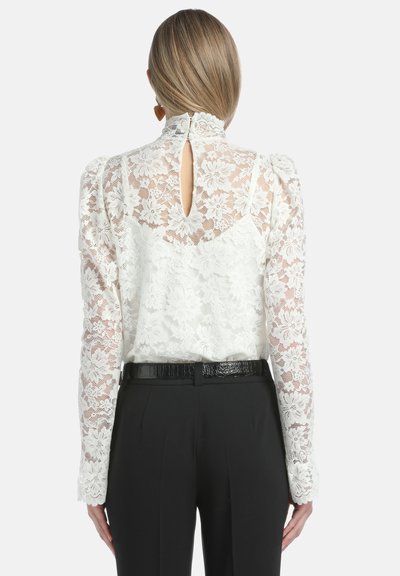 Witte kanten blouse met lange, opgezette mouwen, hoge kraag, sleufdetail op de rug, gecombineerd met zwarte high-waisted broeken en een glanzende zwarte riem.