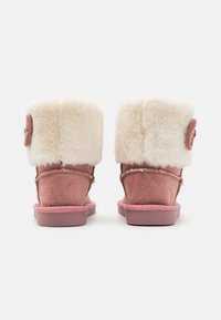 Bottines en daim rose avec un revers en fausse fourrure blanche et un bouton décoratif sur le côté. Semelle en caoutchouc texturé pour une bonne adhérence.