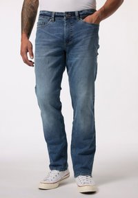 Vaqueros de denim azul claro con corte recto, cinco bolsillos y cierre de botón. Llevados con zapatillas blancas. Presentan un ligero desgaste y un ajuste relajado.