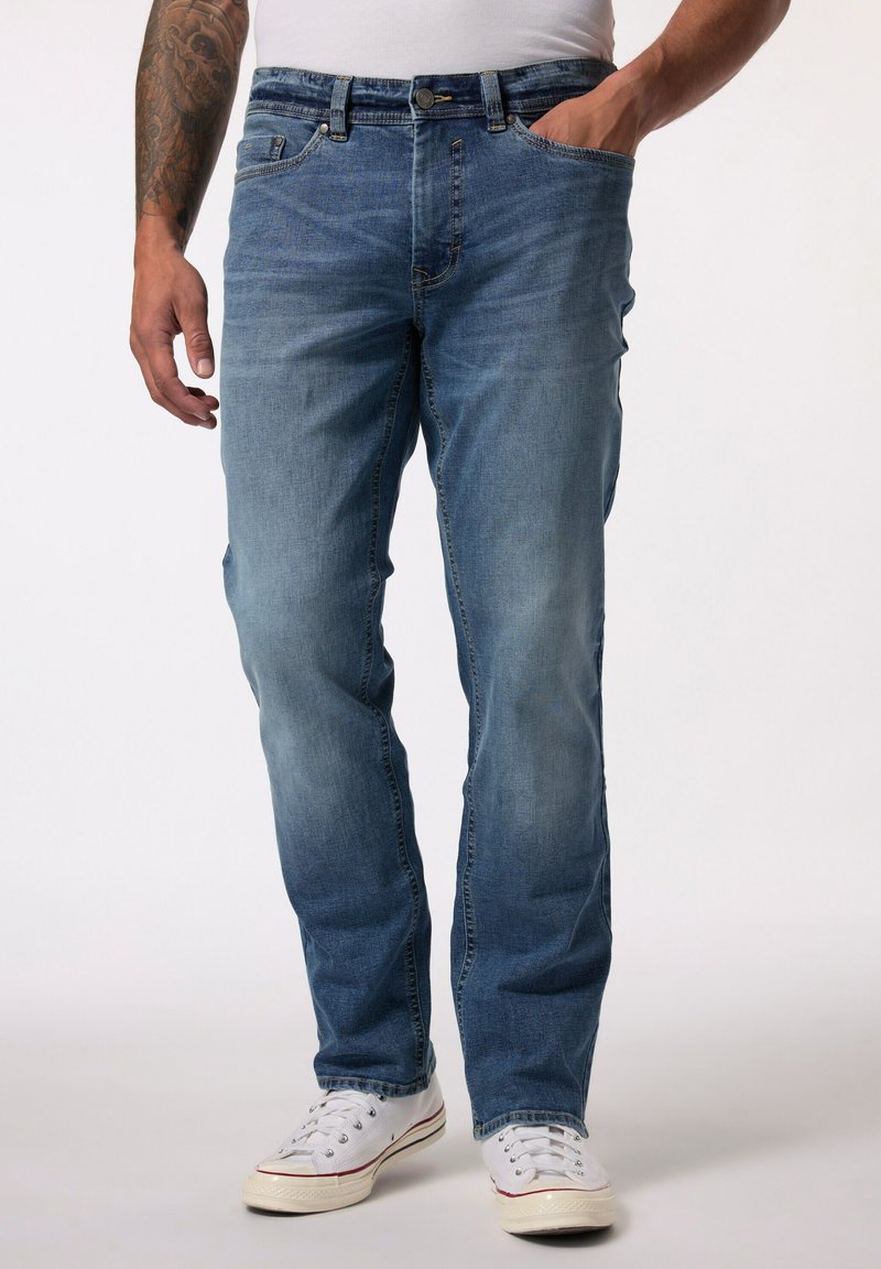 Vaqueros de denim azul claro con corte recto, cinco bolsillos y cierre de botón. Llevados con zapatillas blancas. Presentan un ligero desgaste y un ajuste relajado.
