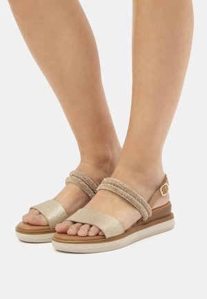 Sandali beige con una fascia frontale glitterata, una fascia centrale intrecciata testurizzata e una fibbia regolabile alla caviglia su una suola imbottita color crema.