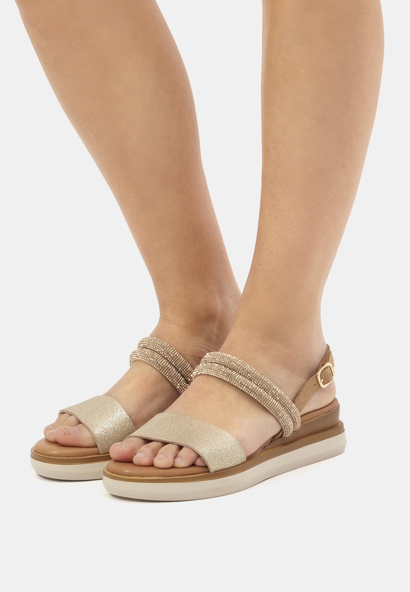 Sandali beige con una fascia frontale glitterata, una fascia centrale intrecciata testurizzata e una fibbia regolabile alla caviglia su una suola imbottita color crema.