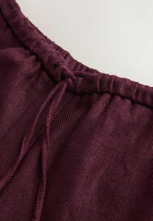 Close-up af en lilla beklædnings elastiske linning med et bundet snoretræk, der viser teksturerede stofdetaljer.