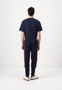 Marineblå t-shirt med korte ærmer, parret med marineblå joggere med kontrasterende brune og hvide sidestriber. Casual pasform, minimalistisk design.