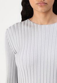Lys grå ribbestrikket genser med rund hals og lange ermer, laget av myk stoff med vertikale striper detaljer.