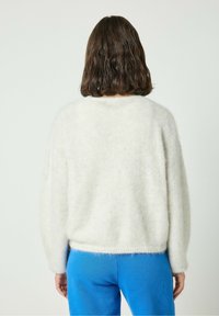 Helles graues, flauschiges Sweatshirt mit rundem Ausschnitt und überschnittenen Schultern, kombiniert mit blauen Hosen. Sanfte Textur mit lässigem Schnitt.