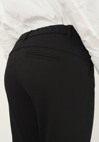 Černé, zakázkové kalhoty s hladkou texturou. Mají dobře padnoucí pas, jednu zadní kapsu a elegantní linie. Vhodné na formální příležitosti.