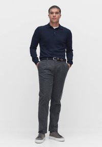 T-paita pitkillä hihoilla merinsinisenä, jossa on kaulus, yhdistettynä räätälöityihin harmaisiin housuihin ja harmaisiin lenkkareihin. Varusteena ruskea vyö, jossa on hopeiset yksityiskohdat.