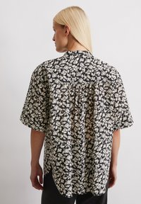 Chemise à imprimé floral en noir et crème ; manches courtes, coupe décontractée, détail de pli dans le dos et ourlet arrondi. Tissu léger à la texture douce.