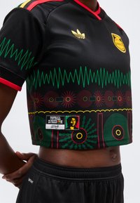 Κοντομάνικη μαύρη αθλητική φανέλα με πράσινα, κόκκινα και κίτρινα γεωμετρικά σχέδια, λογότυπο Adidas, επιγραφή "Το ποδόσφαιρο είναι ελευθερία" και μαύρο σορτς.