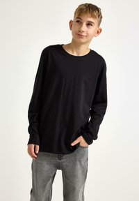 Sort langærmet T-shirt lavet af blødt stof, med rund halsudskæring og afslappet pasform, parret med lysegrå denimbukser.