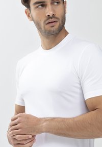 T-shirt bianca a maniche corte con scollo rotondo, realizzata in morbido cotone, indossata da una persona con le mani giunte.