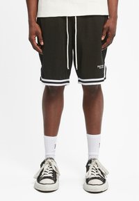 Svarte mesh-shorts med hvite detaljer og snøring. Har en logo på forsiden og kontrasterende horisontale striper ved kanten.