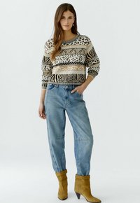 Strickpullover mit Tiermuster in Beige, Schwarz und Braun, kombiniert mit hellblauen, taillierten Jeans und gelben Wildleder-Stiefeletten.