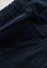 Tissu texturé bleu marine foncé avec coutures surpiquées et taille élastique froncée, montrant des détails en gros plan du matériau et de la confection.