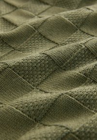 Gros plan d'un tissu tricoté vert olive avec un motif damier texturé de carrés à mailles lisses et ouvertes alternées.