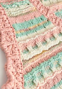 Gros plan d'un tissu tricoté avec des motifs texturés en rose pastel, vert, blanc et jaune, présentant des détails tissés verticaux et horizontaux.